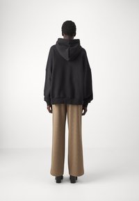 Svart oversized hettegenser med hette, kombinert med beige vid bukser med en subtil mønster. Svart plattform ankelstøvler.