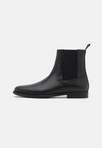 Bottes noires en cuir avec panneaux latéraux élastiques, bout arrondi, texture lisse, et talon bloc bas. Comprend une languette de tirage à l'arrière.