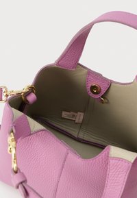 Ροζ τσαντάκι χειρός από δερματίνη με υφή, με χρυσά μεταλλικά στοιχεία, ανοιχτό πάνω μέρος που αποκαλύπτει εσωτερικό σε μπεζ χρώμα και μικρή εσωτερική ετικέτα.