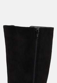 Stivale alla caviglia in suede nero con una texture liscia, asta alta e chiusura con zip laterale per una facile vestibilità.