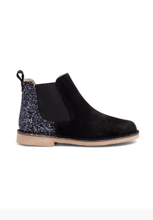 Zwarte suede enkellaars met glanzend zwarte accent op de hak, elastische zijpanelen en een lichtbruine rubberen zool. Rond neusontwerp.