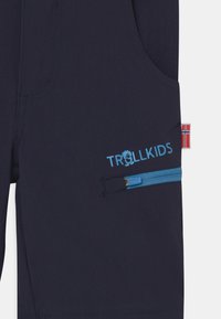 Pantaloni corti navy realizzati in tessuto texturizzato, dotati di una tasca con zip blu e logo "TROLLKIDS". Include un accento con la bandiera norvegese.