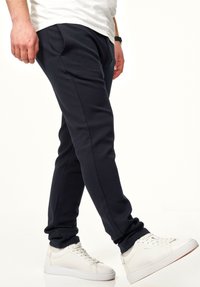 Marineblaue Jogginghosen mit schmalem Schnitt, aus weichem Stoff; ausgestattet mit Seitentaschen und elastischen Bündchen an den Knöcheln, kombiniert mit weißen Sneakers.