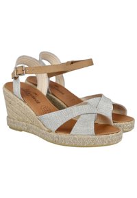 Sandalias de cuña con una plataforma de yute trenzado de color natural, parte superior de tela plateada y correa ajustable en tono marrón claro para el tobillo. Diseño de tiras cruzadas.