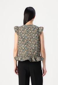 Blusenshirt mit floralem Motiv in Braun, blauen und cremefarbenen Akzenten, kurzen Rüschensäumen und einem Peplum-Saum, kombiniert mit schwarzen Hosen.