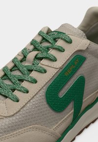 Μπεζ αθλητικό παπούτσι με υφασμένο επάνω μέρος, πράσινα πλεκτά κορδόνια και πράσινο λογότυπο από καουτσούκ. Διαθέτει επενδεδυμένο κολάρο και επίπεδη σόλα από καουτσούκ.