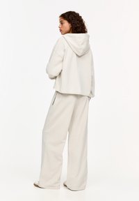 Lichtgrijze cropped hoodie met een trekkoordkap, gecombineerd met wijde broekspijpen. De stof lijkt zacht met een gladde, iets gestructureerde afwerking.