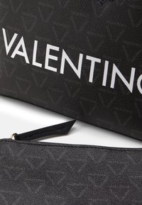 Accessorio in pelle nera testurizzata con un motivo a logo ripetuto, con la scritta "VALENTINO" in bold bianco sul davanti.