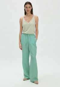 Hellgrünes gestreiftes Tanktop mit V-Ausschnitt, kombiniert mit lockeren, einfarbigen mintgrünen Hosen, die einen elastischen Bund und eine Kordel haben.