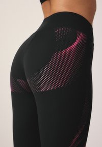 Svarta leggings med en slät textur som har ett rosa prickmönster längs ena sidan, vilket framhäver en atletisk design och en figurnära silhuett.