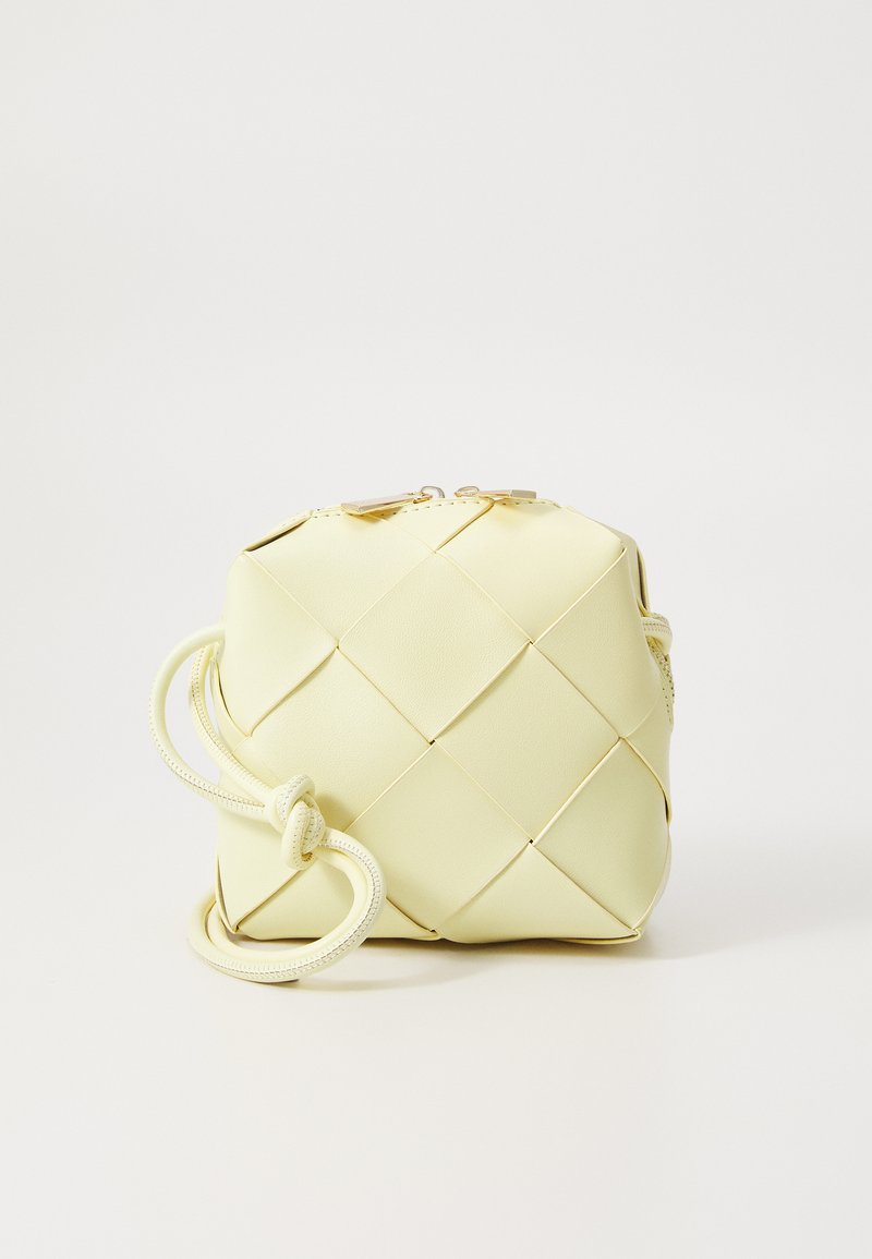 Yellow, woven handbag with a square design, featuring a smooth texture, decorative knotted strap, and gold-tone hardware.