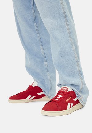 Czerwone zamszowe trampki z białymi akcentami i sznurowadłami, z logo na języku. Połączone z jasnoniebieskimi, lekko oversize'owymi spodniami dżinsowymi.
