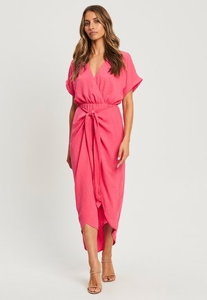 Vestido rosa de estilo envolvente con mangas cortas, una cintura elástica y un lazo en la parte delantera. La tela es ligera, con una textura suave y una silueta fluida.