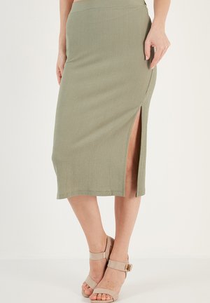 Jupe midi côtelée verte kaki avec une fente latérale et une texture subtile. Associée à des talons beiges à lanières.