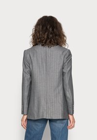 Grijze pied-de-poule blazer met gestructureerde schouders, enkele achterventilatie en zilveren knoopaccenten. Gestructureerde stof met een getailleerde pasvorm.