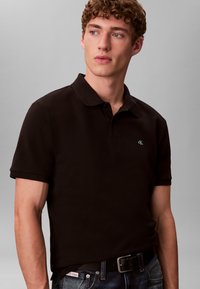 Μαύρο μπλουζάκι πόλο από βαμβάκι με γιακά και κοντά μανίκια. Διαθέτει μικρό πράσινο λογότυπο στο αριστερό στήθος και κλασική εφαρμογή.