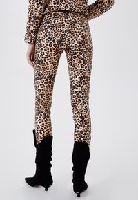 Jeans ajustados de estampado de leopardo en beige y marrón, con una cintura alta, bolsillos traseros, y combinados con botas de ante negras hasta la rodilla.