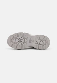 Suola di una scarpa con superficie in gomma strutturata, di colore grigio chiaro, con motivi di battistrada angolari e logo del marchio sulla zona intermedia.