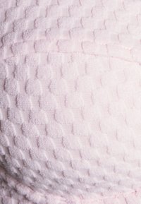 Tecido texturizado em rosa claro com padrão quadriculado, apresentando quadrados suaves e elevados, criando uma superfície tátil.
