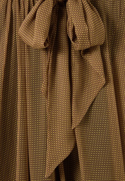 Tela a cuadros en marrón y amarillo con una superficie texturizada, que presenta un destacado detalle de lazo, cayendo suavemente y creando movimiento.