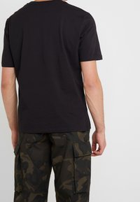 Zwart katoenen T-shirt met korte mouwen, voorzien van een ronde hals en een gladde textuur, gecombineerd met donkere cargobroeken met patroon.