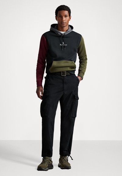 Capuchon sweatshirt met grijs, groen en bordeaux kleurblok. Zwarte cargobroek met zakken. Olijfgroene sneakers met gestructureerde zolen.