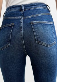 Jeans de mezclilla azul de cintura alta, con una textura suave, dos bolsillos traseros y costuras en contraste en las costuras.