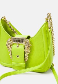 Jasnozielona skórzana torebka z złotym łańcuszkowym paskiem i ozdobną złotą klamrą z wygrawerowanym logo „Versace Jeans Couture”.