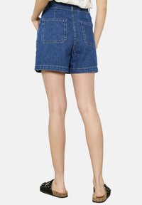 Denim šorti vidēji zilā krāsā ar augstu jostasvietu, sarullētu apakšmalu, divām aizmugurējām kabatām un smalkiem izšuvumiem. Pārī ar ikdienišķām melnām čības.