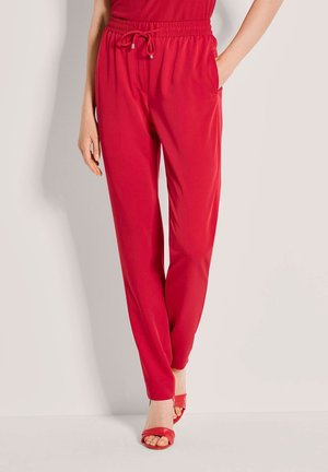 Rote Hose mit Kordelzug und lockerem Schnitt, mit Seitentaschen und zulaufenden Beinen. Hergestellt aus glattem Stoff mit leichter Textur.