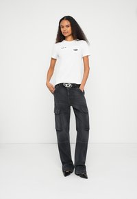 Hvit bomulls t-skjorte med grafiske detaljer, kombinert med svarte cargobukser med lommer og sydd dekorasjon, fullført med et mørkt belte.