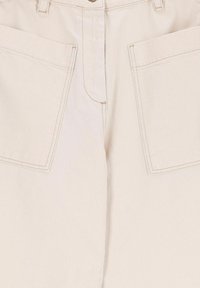 Pantalon en denim beige avec fermeture éclair, deux grandes poches avant et détails de couture visibles. Le tissu a une texture robuste.