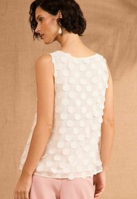Top leggero senza maniche in crema con applicazioni circolari testurizzate e in rilievo. Tessuto morbido, scollo rotondo e design fluido.