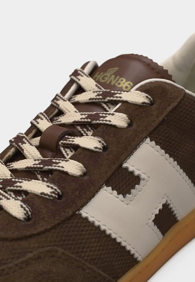 Καφέ αθλητικό παπούτσι με κορδόνια σε μπεζ και καφέ σχέδιο, μπεζ λογότυπο "H" στο πλάι και χρυσή επιγραφή "HGN86" στη γλώσσα.