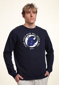 Felpa blu navy con un logo rotondo che presenta un grafiche di un diavolo blu e il testo "PARK FIELD BLUE HILL DEVILS 1967" in bianco. Tessuto misto cotone.