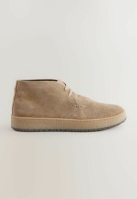 Bottine en suède beige, à bout rond, avec deux œillets pour les lacets, des détails cousus et une semelle en caoutchouc texturé.