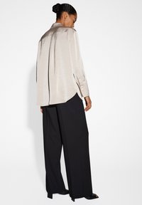 Camicia di satin beige chiaro con maniche lunghe, polsi abbottonati e vestibilità rilassata, abbinata a pantaloni neri a gamba larga e tacchi aperti.
