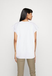 Top blanco de manga corta con un corte relajado. Diseño simple con cuello redondo y material de algodón suave. Espalda limpia y sin costuras.