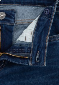 Denimist teksapüksid tõmbluku ja nööbiga, tumeda pesuga, kuldse tõmblukuga ja hele sinise kangase voodriga vöökohas.