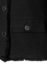 Zwarte textuurjacket met een gerafelde onderrand, zilveren drukknoopsluitingen en een borstzak met een klep. De stof lijkt zacht en licht pluizig.