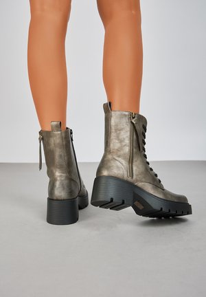Bottines grises métalliques avec une finition texturée, présentant un laçage à l'avant, une fermeture éclair sur le côté et un talon noir épais pour la stabilité.