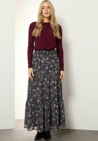 Bordeaux lange mouwen top gecombineerd met een zwarte maxi rok met bloemenpatroon, met een smocked taille en gelaagde ruffle zoom. Zwarte laarzen maken de outfit compleet.