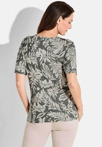 Kortom shirt met korte mouwen in donkergroene stof met een lichtbeige, botanisch bladerenpatroon; ronde halslijn en een licht gebogen zoom aan de achterkant.