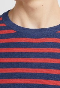 Marineblau und rot gestreifter Pullover mit geripptem Rundhalsausschnitt; stricktextur mit gleichmäßigem Abstand zwischen den Streifen. Weiches Stoff-Aussehen.