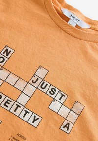 Oranges Baumwoll-T-Shirt mit einem Kreuzworträtsel-Design in Schwarz und Weiß, verziert mit Glitzerakzenten. Rundhalsausschnitt und strukturiertem Stoff.