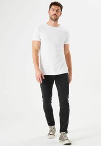 Camiseta blanca de manga corta combinada con jeans negros ajustados y zapatillas grises, con un diseño de cuello redondo sencillo.