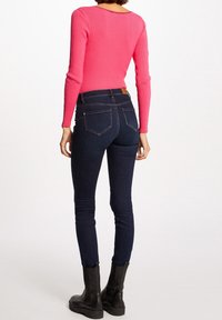 Dopasowany różowy prążkowany sweter z długimi rękawami, zestawiony z ciemnymi obcisłymi jeansami z tylnymi kieszeniami oraz czarnymi botkami za kostkę.