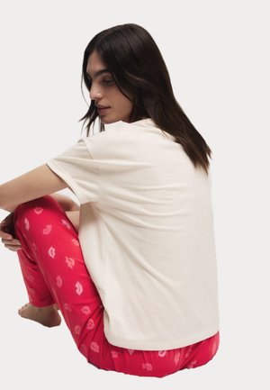 Crème kleur t-shirt met korte mouwen, gecombineerd met roze pyjamabroeken met een kusprint. Relaxte pasvorm met een zachte textuur.