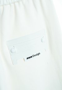La tela blanca presenta una etiqueta texturizada con letras en relieve y un acento circular, mostrando "MWM Design" y detalles adicionales en relieve.