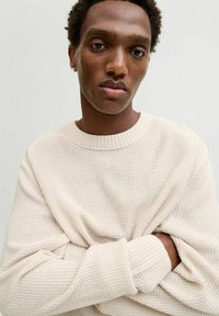 Cream-colored knitted sweater features a textured pattern, ribbed neckline and cuffs, with a relaxed, oversized fit that drapes comfortably.